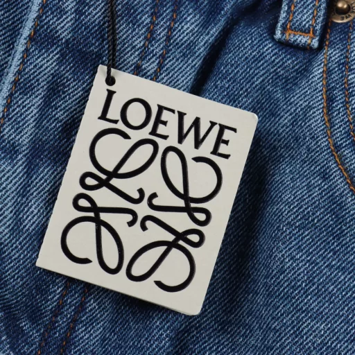 Loewe Anagram denim trousers with denim embroideryThe tight double core yarn is used, the knee is decorated with laser cutting Anagram, the classic LOEWE leather label is embellishments, laser cutting, the pants are manually opened, laid out flat to make laser cutting Anagram pattern, and then the inner cloth is affixed manually and the daily output is low. The labor cost is expensive, the loss is high, and the daily output is low. The special desizing agent is preferred, and then the cloth is soaked in it and then rinsed evenly, loose version