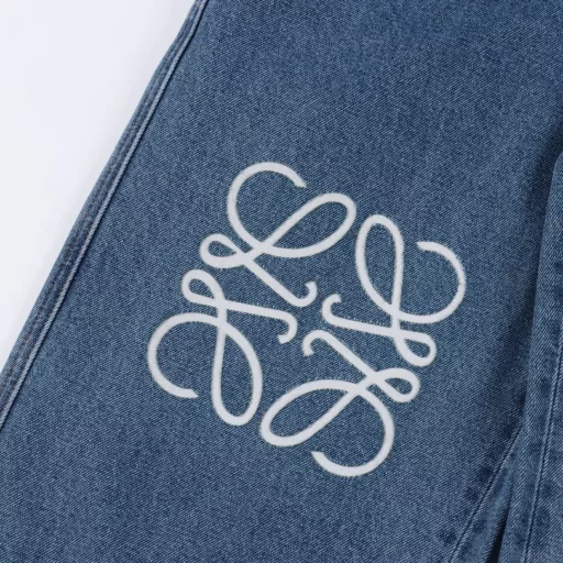 Loewe Anagram denim trousers with denim embroideryThe tight double core yarn is used, the knee is decorated with laser cutting Anagram, the classic LOEWE leather label is embellishments, laser cutting, the pants are manually opened, laid out flat to make laser cutting Anagram pattern, and then the inner cloth is affixed manually and the daily output is low. The labor cost is expensive, the loss is high, and the daily output is low. The special desizing agent is preferred, and then the cloth is soaked in it and then rinsed evenly, loose version
