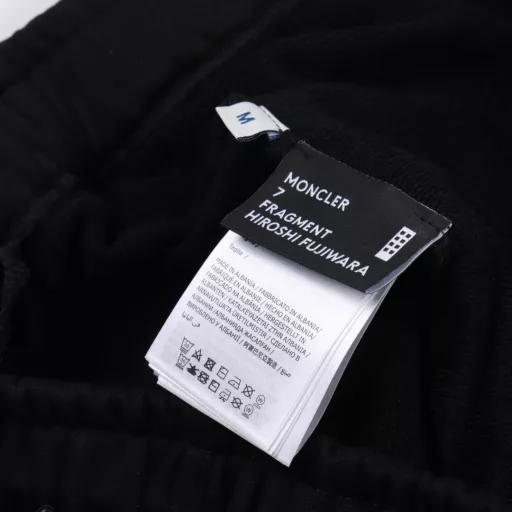 MC MOCLER X Hiroshi Fujiwara Joint Badge ShortsMade of 100% pure cotton, the surface is treated with fleece to form a cotton fleece fabric, which has a soft and delicate touch and evenly distributed fluff. The natural structure of cotton fiber provides good moisture absorption and perspiration ability, is skin-friendly and non-irritating, and is also lightweight, making it burden-free to wear. The MOCLER&FRGMT embroidery process is used on the back pocket. The double-thread winding structure makes the embroidery surface thick and not easy to wear. The stitches are hidden on the back of the fabric, without messy threads, which improves durability and aesthetics. The letters starting with G27507 are decorated under the side pocket using the glue printing process, which has a three-dimensional visual effect and a bumpy and soft texture. It is not easy to fall off through high-temperature foaming. Customized accessories